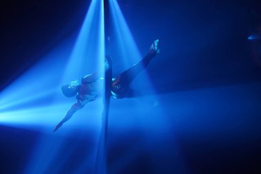 Brezilyalı güçlü seksi adam mavi ışıklarda hava ipekleriyle performans sergiliyor. Spor salonu ve yaşam tarzı konsepti. Siyah arka plan. Hava ipeklerinin üzerine düş