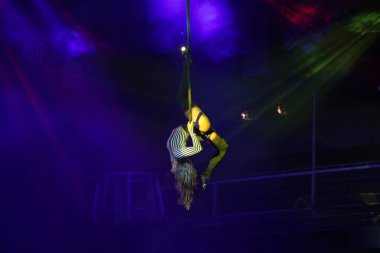 Esnek genç kadın hava çemberinde performans sergiliyor, hava çemberinde esnek duruyor, hava sirki gösterisi, sarı mavi mavi ışık. Esnek kadın jimnastikçi potada baş aşağı duruyor. Gece kulübü performansı