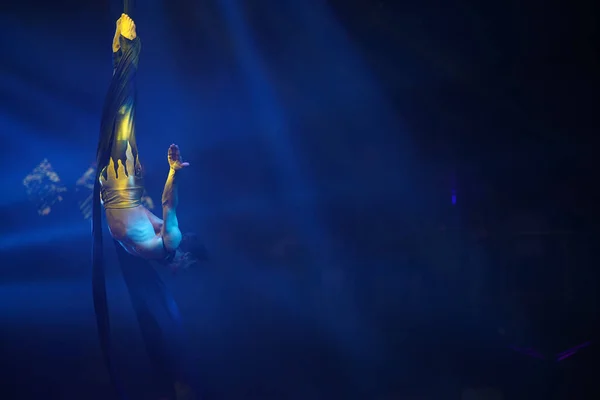 巴西性感男人在蓝灯的空中丝绸上表演 运动训练馆和生活方式的概念 黑色背景 胸腺倒挂在空中丝绸上 — 图库照片