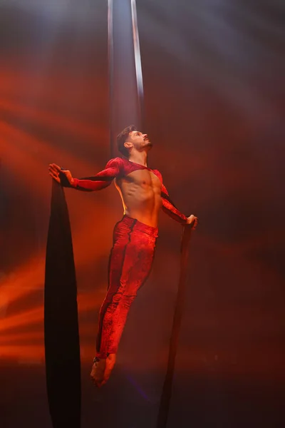 Brezilyalı güçlü seksi adam kırmızı ışıklarda hava ipekleriyle performans sergiliyor. Spor salonu ve yaşam tarzı konsepti. Siyah arka plan. Güçlü dur.