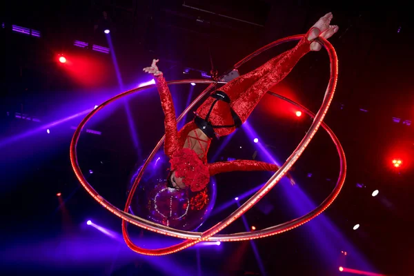 Esnek genç bir kadın, hava çemberinde performans sergiliyor. Hava çemberinde esnek duruyor. Hava sirki gösterisi, mavi ve kırmızı ışık. Esnek kadın jimnastikçi potada baş aşağı duruyor. Gece kulübü performansı