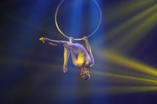 Flexible young woman make performance on aerial hoop, flexible back on aerial hoop, aerial circus show, yellow light. Flexible woman gymnast upside down on hoop. Show in night club