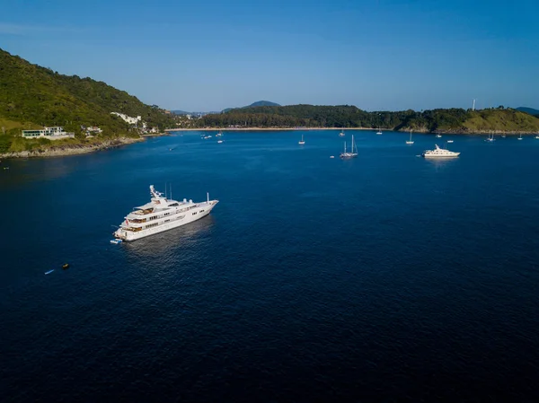 Kar beyazı büyük bir yat yeşil tepeler ve küçük gemilerle çevrili pitoresk bir körfezde duruyor, Nai Harn Sahili, Phuket, Tayland