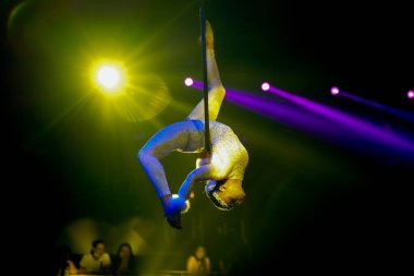 Esnek kadın jimnastikçi, havadaki halka arka ışıklandırma sarı ve mor ışıklarda baş aşağı performans sergiliyor..