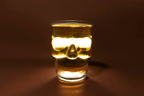 Refreshing and cold glass of beer shaped like skull isolated over brown background in a studio shot. Hallowen concept.