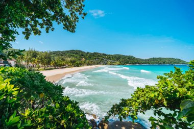 Tropical beach wiht long waves for surf framed by green leaves. Summer vacation and nature travel adventure concept.. Summer composition. High quality photo