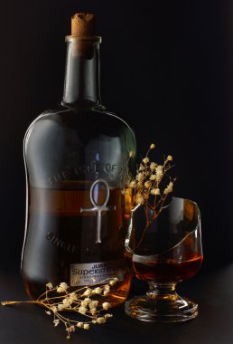 Natürmort bir şişe viski, bir siyah arka plan üzerinde kırık cam ve kuru çiçekler