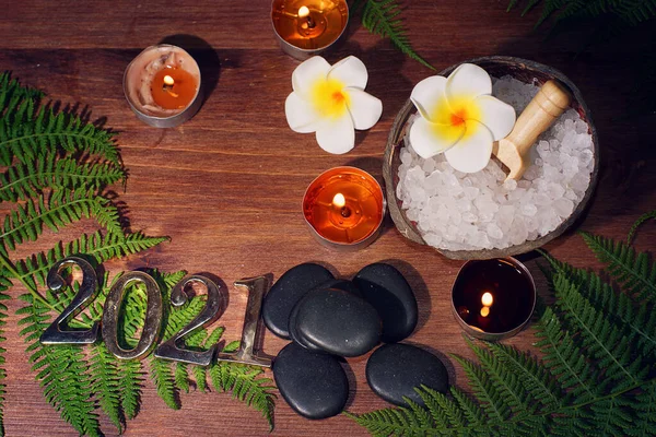 Pierres noires de basalte pour massage chaud, sel de mer pour épluchage, bougies allumées et numéros 2021 sur la table Images De Stock Libres De Droits
