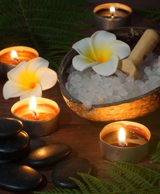 Sıcak masaj için siyah düz taşlar. Arka planda yanan mumlar ve SPA prosedürleri için setler..