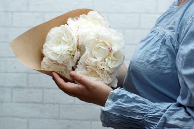 Kadın elleri bir buket pembe şakayık tutuyor.