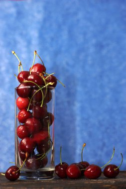 Olgun kirazlı bir bardak mavi bir tahtanın yanında duruyor.