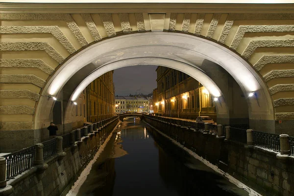 Arch over the river with reflective lanterns and buildings in a winter evening — Stock Photo, Image