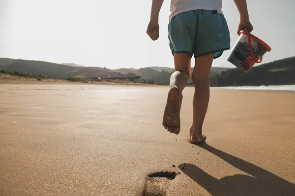 Çocuk sahilde yürüyor ve ayak izleri bırakıyor.