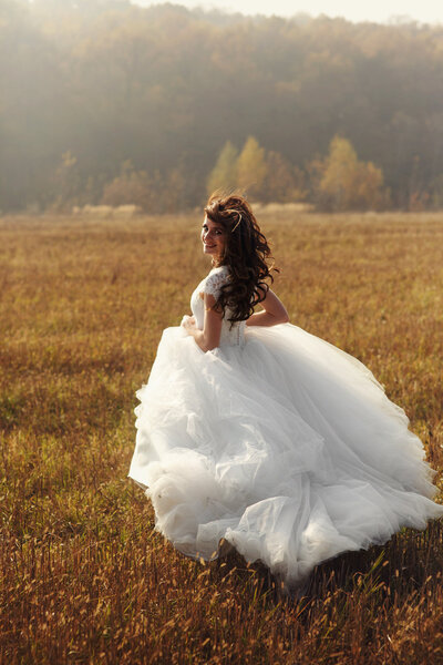 Beautiful happy brunette bride in white dress running in sunset field freedom