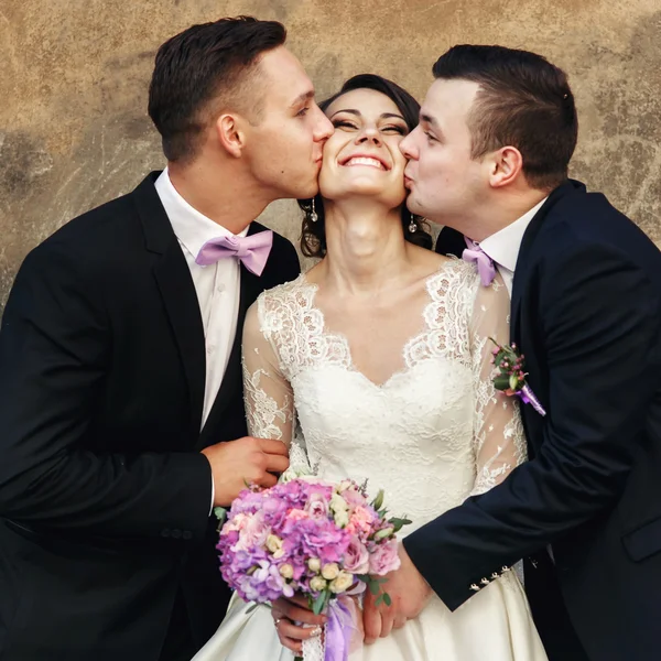 Dois noivos bonitos beijando noiva — Fotografia de Stock