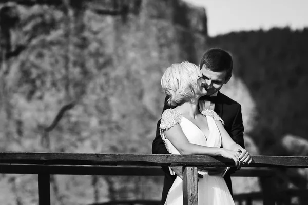 Sposo viene alla sposa in piedi vicino alla recinzione sulla montagna — Foto Stock