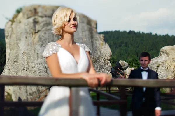 Novio viene a la novia de pie cerca de la valla en la montaña —  Fotos de Stock