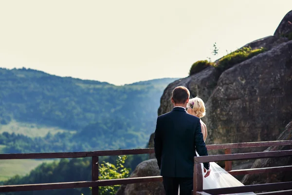 Novio viene a la novia de pie cerca de la valla en la montaña —  Fotos de Stock