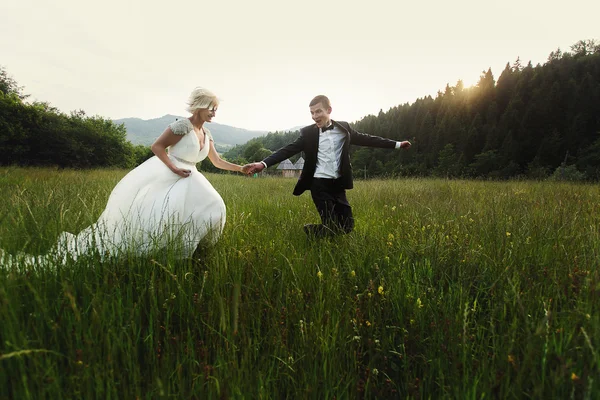 Wedding couple running on green grass at sunset — Stock Photo, Image