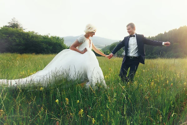 Pareja de boda corriendo sobre hierba verde al atardecer — Foto de Stock