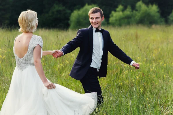 Casamento casal correndo na grama verde ao pôr do sol — Fotografia de Stock