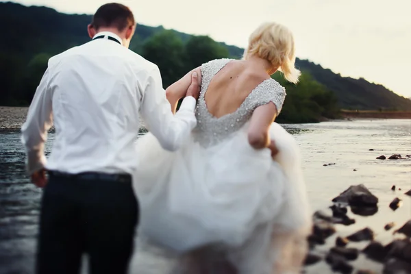 Sposa e sposo passeggiando vicino al fiume al tramonto — Foto Stock