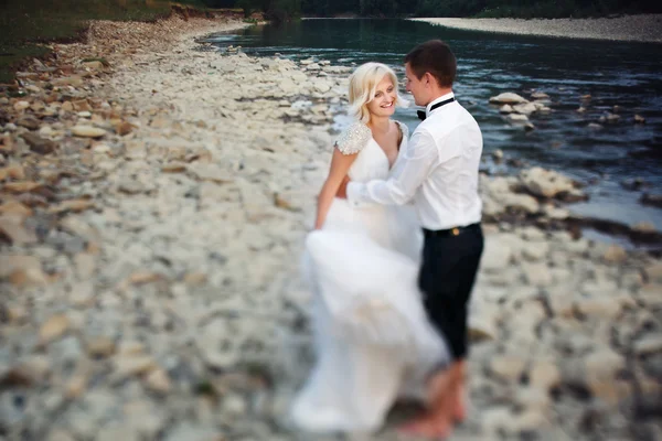 Bride and groom walking near the river at sunset — Stock Photo, Image