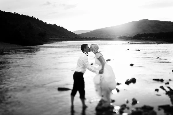 Bride and groom walking near the river at sunset — Stock Photo, Image