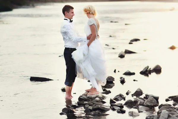 Sposa e sposo passeggiando vicino al fiume al tramonto — Foto Stock