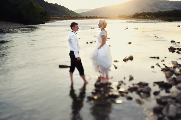 Bride and groom walking near the river at sunset — Stock Photo, Image