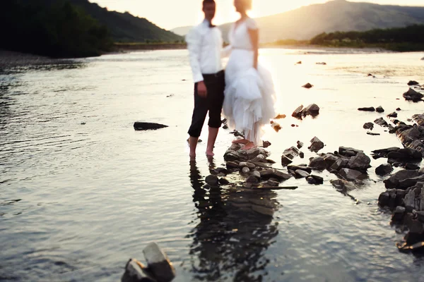 Novia y novio caminando cerca del río al atardecer — Foto de Stock