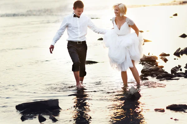 Mariée et marié marchant près de la rivière au coucher du soleil — Photo