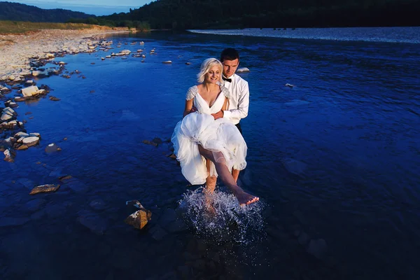 Bröllopsparet körs på grönt gräs vid solnedgången — Stockfoto