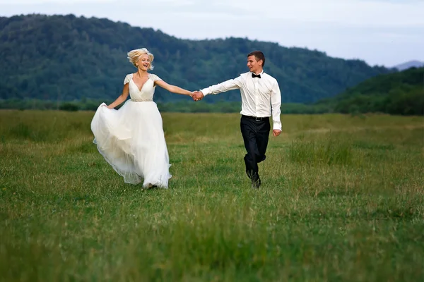 Casamento casal correndo na grama verde ao pôr do sol — Fotografia de Stock