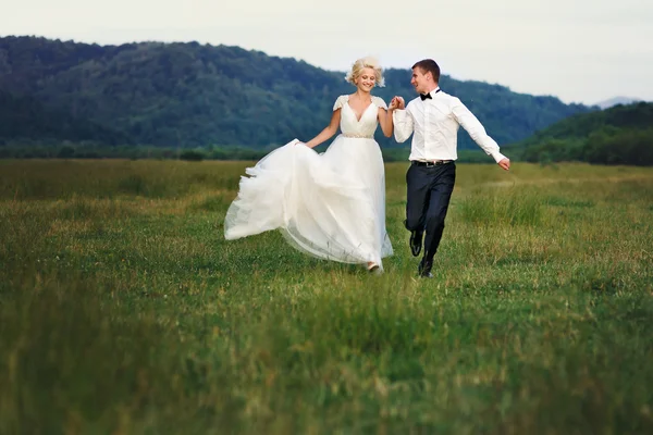 Wedding couple running on green grass at sunset — Stock Photo, Image