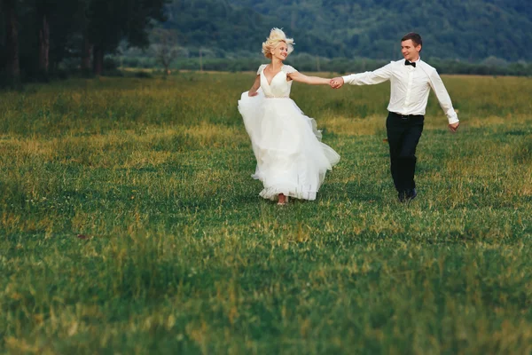 Casamento casal correndo na grama verde ao pôr do sol — Fotografia de Stock