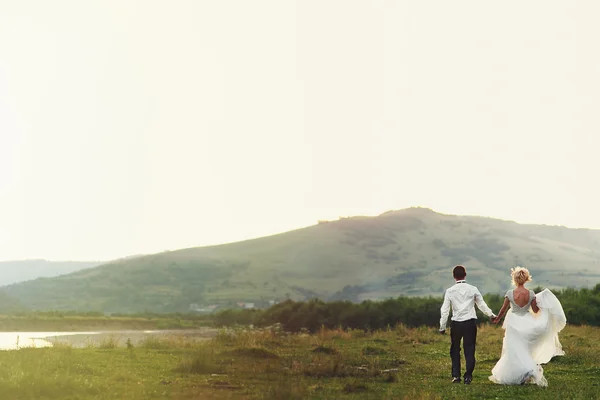 Wedding couple running on green grass at sunset — Stock Photo, Image