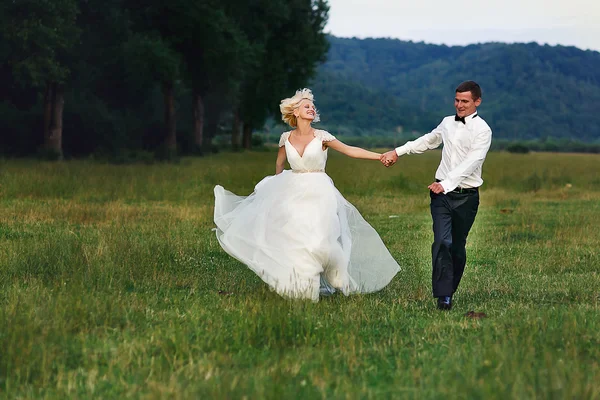 Pareja de boda corriendo sobre hierba verde al atardecer — Foto de Stock