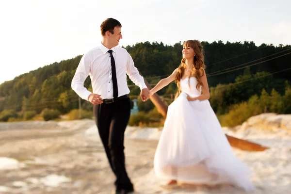 Braut und Bräutigam halten sich an den Händen und rennen durch den Sand. — Stockfoto
