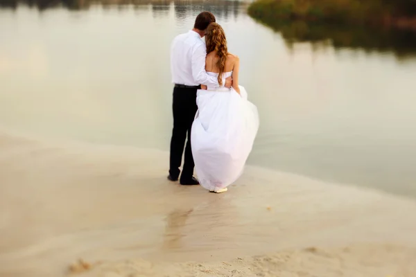 Braut und Bräutigam stehen am Rande des Strandes und schauen hinein. — Stockfoto