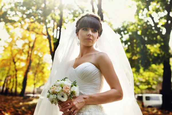 Невеста с букетом, стоящей на солнце в парке — стоковое фото