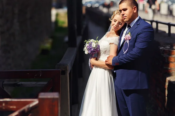 A noiva e o noivo com um buquê em pé ao sol e perto — Fotografia de Stock