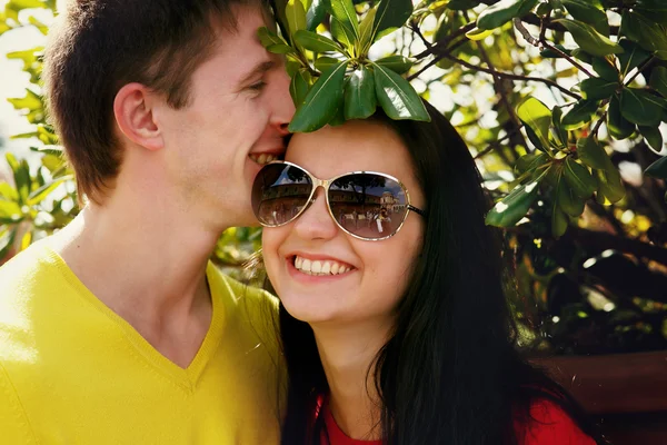 Усміхнена пара обіймається зовні серед кущів в сонячний день — стокове фото