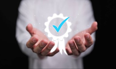 Parlak bir onay rozeti sunan eller, kalite güvencesini, güveni, onaylanmayı, onaylanmış standartları ve mesleki mükemmelliği sembolize eder..