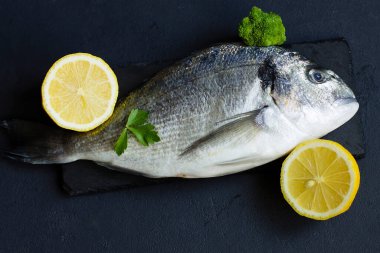 Taze, çiğ gilthead, limon ve otlarla, kesme tahtasının üzerinde. Gri arka plan. Üst görünüm.