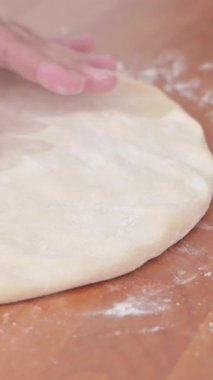 Woman baker is rolling out dough using wooden rolling pin on cozy wooden table. She is rolling dough in flour, preparing it for an Italian pizza with tomato and cheese. High quality 4k footage