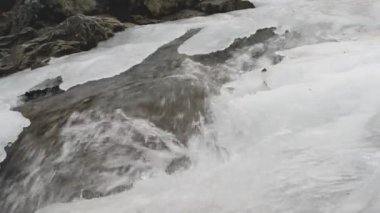 Güçlü bir dağ şelalesi. Buz erir ve su buz örtüsünün altından akar. Bahar geliyor. 4k video.