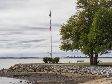 Bir bayrak direği, Delaware Şehir Rafinerisi 'ne tepeden bakan New Castle Battery Park' ta bulutlu bir gökyüzünde Amerikan bayrağı dalgalandırıyor..