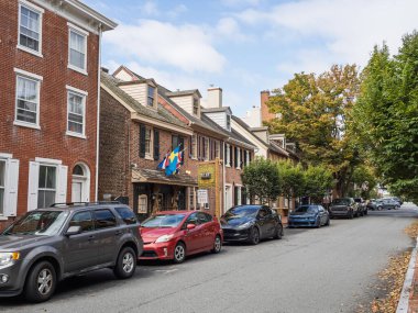 Bir dizi tarihi kırmızı tuğla koloni evi New Castle, Delaware 'de güneşli bir günde kaldırım kenarına park edilmiş çeşitli modern arabalarla bir cadde hizasında..