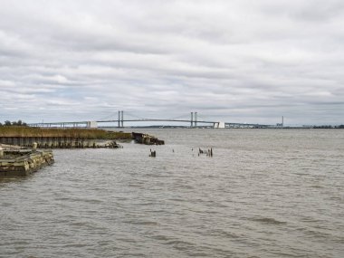Bulutlu bir sonbahar gününde New Castle rıhtımının kırsal ve aşırı gelişmiş bir bölümünden Delaware Anıt Köprüsü manzarası.